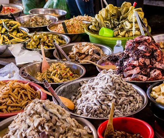 Kamboçya Mutfağı Kamboçya, Güneydoğu Asya’da Mekong Nehri ve Tonle Sap Gölü’nün kesişim noktasında yer alır. Bu stratejik konum, Kamboçya mutfağının hem Çin hem de Tayland mutfaklarından etkilenmesine olanak tanımıştır. Pirinç ve balık, mutfağın temel öğelerini oluştururken, taze otlar ve baharatlar yemeklere karakter kazandırır. Kamboçya mutfağı, hem geleneksel hem de modern öğeleri harmanlayarak zengin bir lezzet deneyimi sunar. Konulu bir haber görseli.