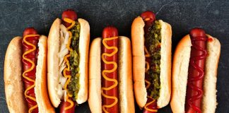 Dünya mutfağında geniş bir yer edinen hot dog, özellikle Amerika Birleşik Devletleri’nde adeta bir sembol haline gelmiştir. Kökeni 19. yüzyılın sonlarına kadar uzanan bu yiyecek, Almanya’dan Amerika’ya göç edenlerin beraberinde getirdiği sosis kültürü ile ortaya çıkmıştır. Uzun ekmek arasına yerleştirilen sosisin seneler içinde farklı soslarla buluşması, hot dog’u bugünkü popüler formuna kavuşturmuştur. Konulu bir haber görseli.