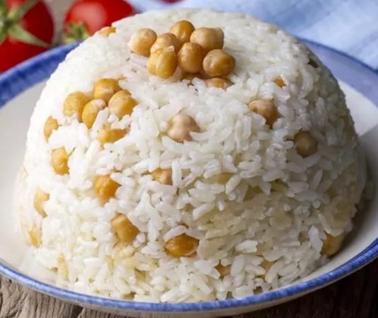 Nohutlu pilav, Türk mutfağının en sevilen ve sık tüketilen yemeklerinden biridir. Hem günlük öğünlerde hem de özel davetlerde sıkça hazırlanır. Tarih boyunca farklı kültürlerin etkisiyle şekillenen bu tarif, hem doyurucu hem de besleyici bir seçenek olarak öne çıkar. Konulu bir haber görseli.