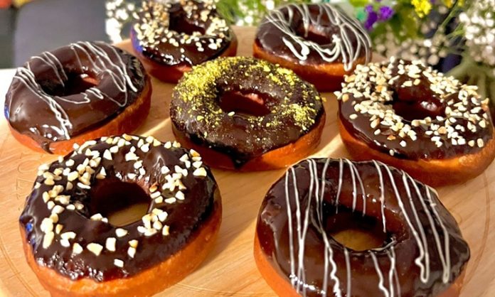 Dünyanın en sevilen tatlılarından biri olan donut, günümüzde yalnızca klasik şekerli halka formundan ibaret değil. Renkli glazeler, çikolata kaplamalar, meyve aromaları ve hatta tuzlu versiyonlarıyla karşımıza çıkan bu tatlı, hem çocukların hem yetişkinlerin ilgisini çekmeye devam ediyor. Özellikle kafe zincirlerinin yaygınlaşmasıyla birlikte donut tercih eden kitlenin her geçen gün arttığı görülüyor. Görsel sunumdaki çeşitlilik, tatlının sosyal medya platformlarında hızla viral olmasına yardımcı oluyor. Konulu bir haber görseli.