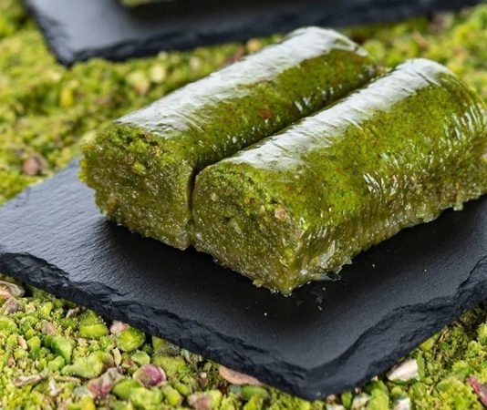 Fıstıklı Sarma Tatlısının Osmanlı’dan Günümüze Uzanan Lezzet Yolculuğu Fıstıklı sarma, Türk tatlı kültürünün hem tarihsel hem damak zevki açısından en özel lezzetlerinden biri olarak biliniyor. Osmanlı saray mutfağından günümüze taşınan zengin mirasın bir parçası olan bu tatlı, özellikle özel günlerde, bayram sofralarında ve davet masalarında sıklıkla tercih ediliyor. Bu nedenle sadece gastronomik bir tatlı olmakla kalmayan fıstıklı sarma, kültürel bir simge haline gelmiş durumda. Şerbetli tatlılar arasında kendine özgü yapısıyla farklı bir yer edinen bu lezzet, hem yapımı hem sunumu hem de ustalığıyla dikkat çekiyor. Konulu bir haber görseli.