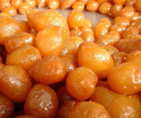 Lokmanın Geleneksel Tat Yolculuğu Sokak Lezzetinden Modern Tabaklara Uzanan Hikâye Türk mutfağının en köklü tatlılarından biri olan lokma, yüzyıllardır hem Anadolu’nun hem de Ege’nin kültürel mirasını taşımaya devam eden özel bir lezzet olarak öne çıkıyor. Özellikle paylaşma, bereket ve toplumsal dayanışmayı temsil eden bu tatlı, günümüzde sadece geleneksel törenlerde değil, modern gastronomi alanında da sıkça tercih edilen bir tat haline geldi. Hafif kabaran hamurunun kızgın yağda altın rengi alması ve ardından şerbetle buluşması, lokmayı eşsiz kılan temel özelliklerden biri. Sokak tezgâhlarının değişmeyen yüzü olan lokma, bugün artık restoranlarda ve kafelerde de farklı sunumlarla yer buluyor. Konulu bir haber görseli.
